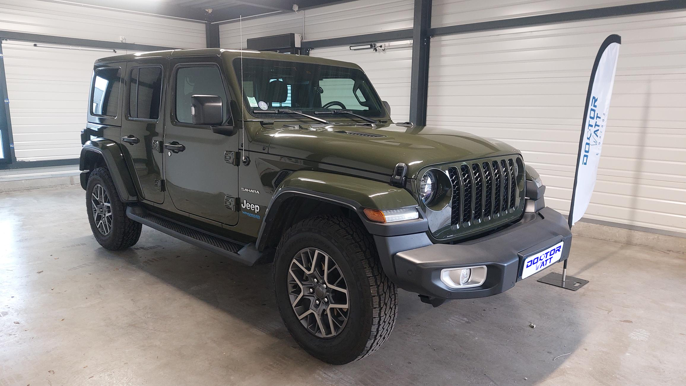 Vue latérale d'une Jeep Wrangler Unlimited Sahara hybride en excellent état, mettant en valeur ses lignes élégantes, ses portes et ses roues.